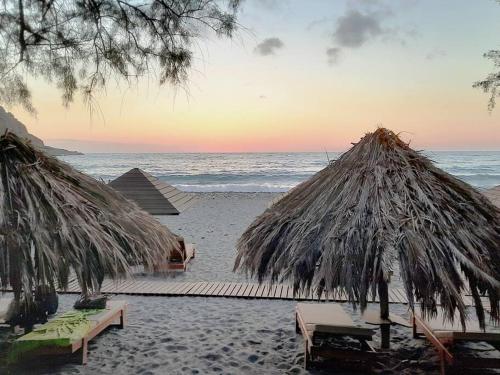 a beach with two umbrellas and chairs and the ocean at Luxurious stone cave with pool and sea view in Kissamos