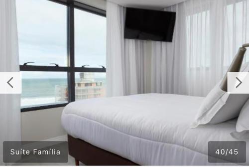 a bedroom with a white bed and a large window at Hotel Boutique Brava Mundo - SC in Itajaí