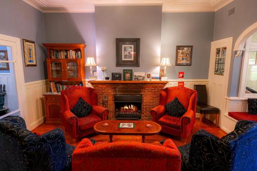 a living room with red chairs and a fireplace at KUBBA ROONGA GUESTHOUSE - Boutique Luxury Spa Retreat & Gardens - Blue Mountains in Blackheath