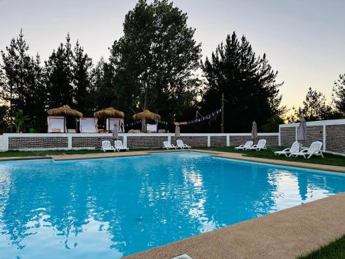 a large swimming pool with white chairs and trees at Complejo bosque escondido in Quillón