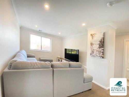 a white living room with a couch and a tv at Scotty’s Place – Luxury Retreat in Inverloch