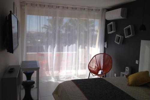 une chambre avec un lit et une fenêtre avec une chaise dans l'établissement Naturiste Cap d'Agde Port Nature 650, au Cap d'Agde