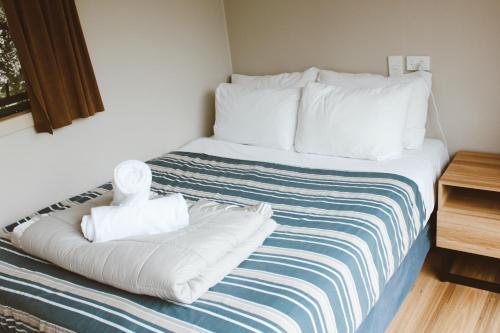 a bed with white sheets and a teddy bear on it at The Barn Cabins & Camp in Marahau