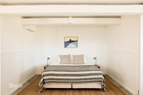 a white bedroom with a bed with a striped blanket at Bluewater on the Beach in Byron Bay