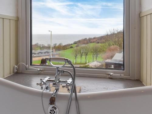 a bath tub with a shower in front of a window at Houndsfield in Ilfracombe