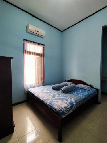 een bed in een blauwe kamer met een raam bij Guest House Djatis Purwo Wasito in Bojonegoro