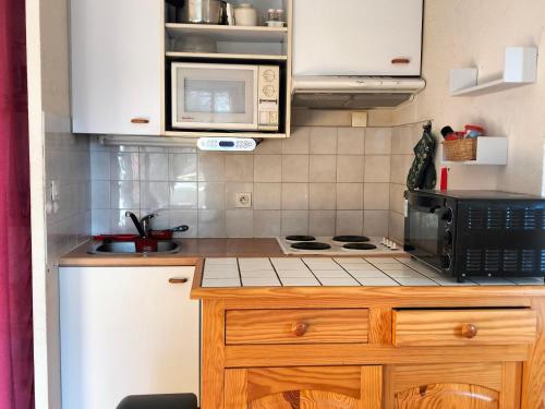 une petite cuisine avec une cuisinière et un micro-ondes dans l'établissement Charmant 2 pièces avec balcon, proche village et navettes, pour 4-6 personnes - FR-1-761-37, à Villard-de-Lans