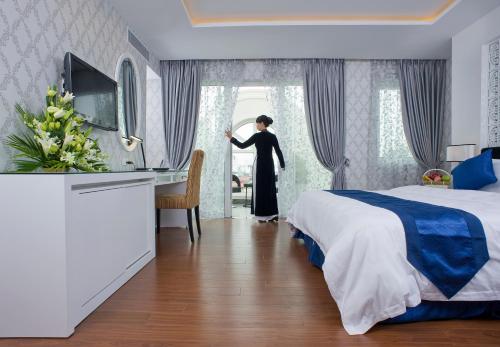 una mujer en una habitación de hotel con cama y escritorio en Victor Gallery Hotel & Restaurant In Hanoi city, en Hanói