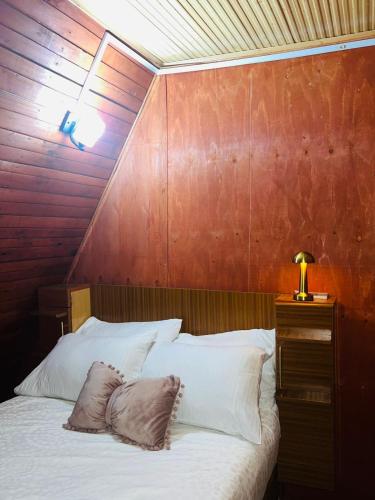 a bed with white pillows and a wooden wall at Aquawood Cabins in Kianyaga