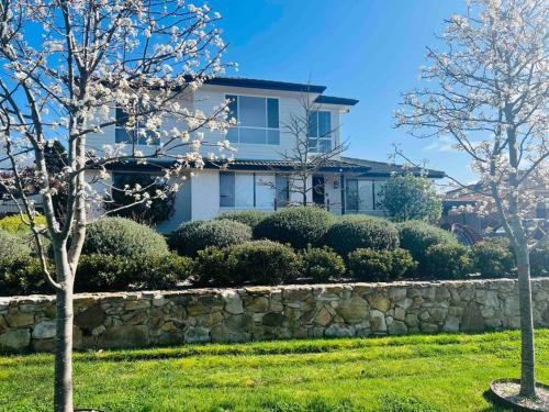 ein weißes Haus mit einer Steinmauer und Bäumen in der Unterkunft Merrett Vale Home in Moss Vale