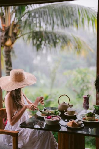a woman in a hat sitting at a table with food at Inara Alas Harum in Ubud