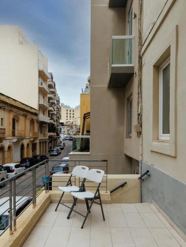 two chairs on a balcony with a city street at Stylish St Julians 2 bedroom apartment for rent in the city centre with Terrace in St. Julianʼs
