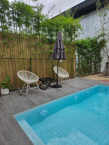 una piscina con 2 sillas y una sombrilla en RINA Poolvilla (รินะ พูลวิลล่า) en Hat Yai