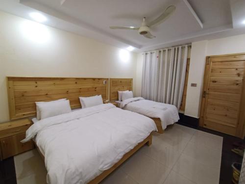 two beds in a bedroom with white sheets at F R Darya e Swat Hotel in Swat