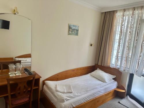 a small bedroom with a bed and a desk and a window at Daf Trans Hotel in Peshtera