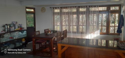 uma sala de jantar com uma mesa e duas janelas em Sunakhari em Darjeeling