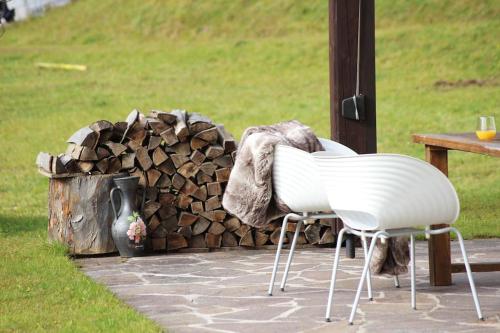 two white chairs sitting next to a pile of fire wood at Das Ferienhaus in Achenkirch in Achenkirch