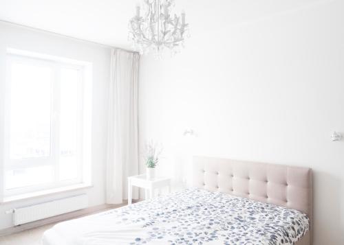 a white bedroom with a bed and a chandelier at Skanstes Apartment Free Parking in Riga