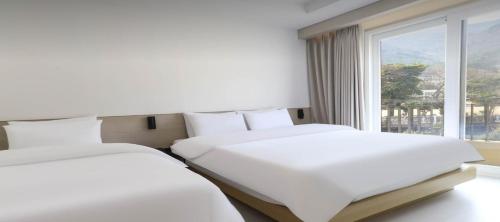 two beds in a hotel room with a window at Geoje Mongdol Beach H Avenue Hotel in Geoje 