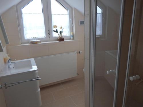 a white bathroom with a shower and a sink at Ferienhaus Dünenblick am Sandstrand in Julianadorp