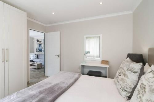 a white bedroom with a large bed and a desk at Modern 1 bedroom non-seafacing unit on luxury golf estate in Knysna
