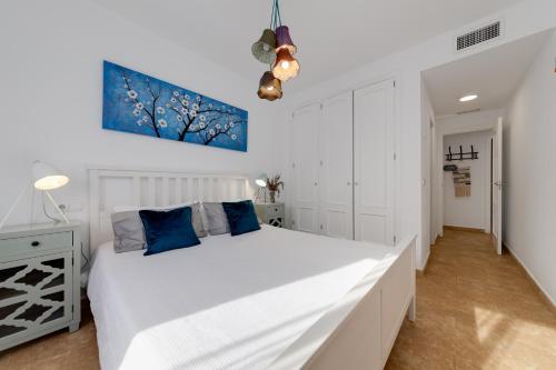 a white bedroom with a large white bed with blue pillows at Mi Patio in Torrevieja
