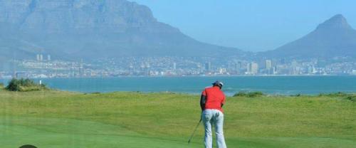 a man standing on a golf course holding a club at Sunset Waves Bloubergstrand in Sunset Beach