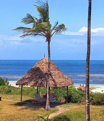 a straw umbrella and palm trees on the beach at Watamu Beach Cottages in Watamu