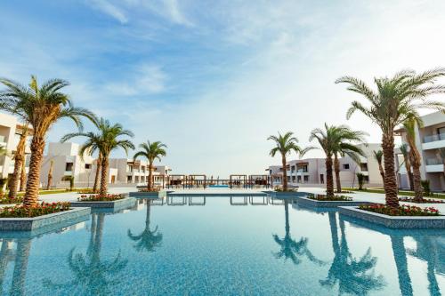 a swimming pool with palm trees and buildings at Jaz Amara in Marsa Alam City