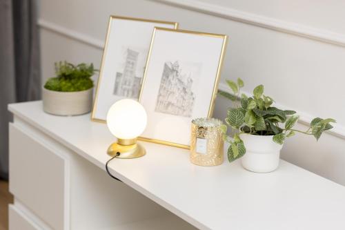 a white shelf with pictures and plants on it at White & Gold Marble Apartment Łódź Fabryczna by Renters in Łódź