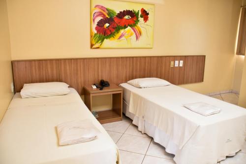 two beds in a room with a painting on the wall at Hotel Casa Nova in Várzea Grande