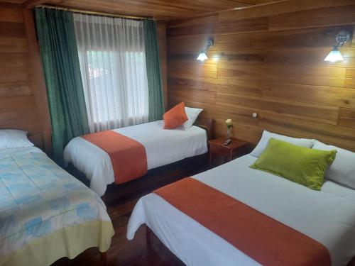 two beds in a room with wooden walls at Finca La Esperanza in Palora