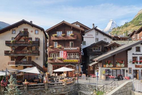 a group of buildings with tables and umbrellas at Hotel Weisshorn in Zermatt