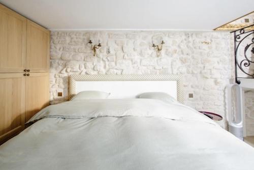a white bed in a bedroom with a stone wall at Le Clos Des Vosges in Paris