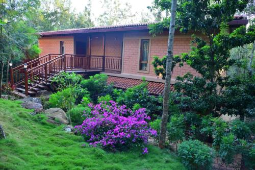 a house with a deck and flowers in the yard at Sereno Barn Eco Stay Chikmagalur in Chikmagalūr