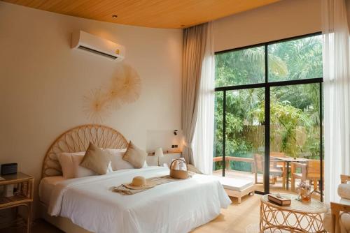 a bedroom with a white bed and a large window at บ้านไร่มีสุข Baanrai Meesuk in Surat Thani