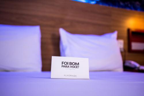 a sign on top of a bed with pillows at Suítes Alvorada in Rio Verde