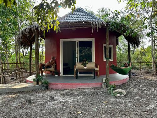 uma casa vermelha com dois homens sentados numa rede lá fora em A Maze Inn Cottage em Phumĭ Chroŭy Svay