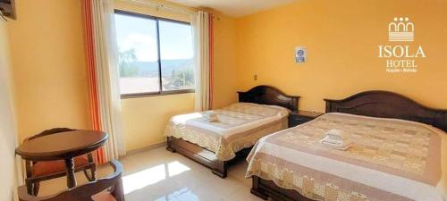 um quarto com duas camas e uma mesa e uma janela em Hotel Isola by Aiquile em Aiquile
