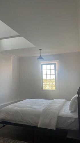a white bedroom with a bed and a window at Prairie in Al Khaznah