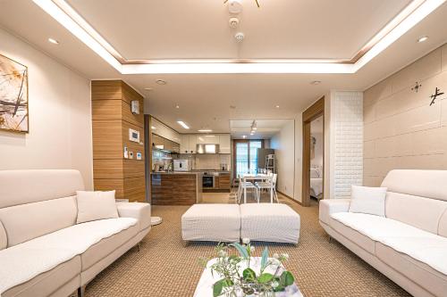 a living room with white couches and a kitchen at Swa Tailored Serviced Home Near Gwanggyo Stn in Suwon