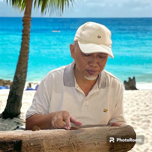 a man wearing a hat sitting on the beach at Home 