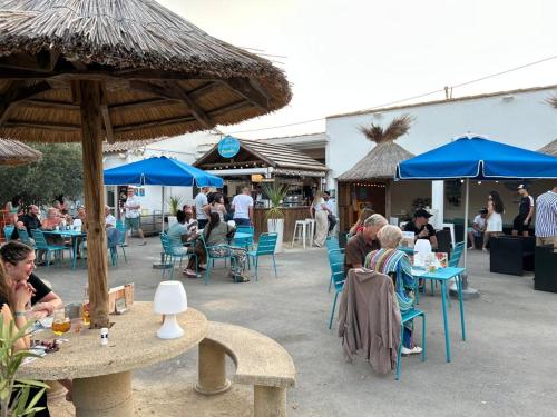 Un groupe de personnes assises à des tables avec des parapluies bleus dans l'établissement Camping Paradis Family les Rives de l'Hérault, à Gignac