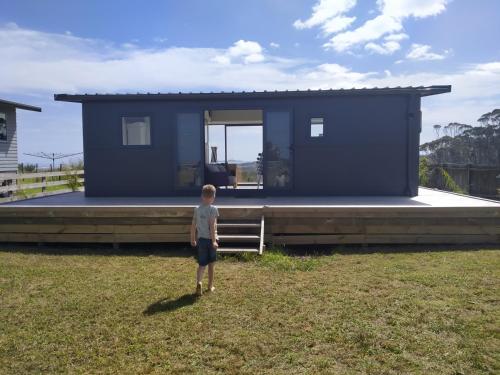 a boy standing in front of a blue house at Seascape Peninsula Bach in Kaitaia