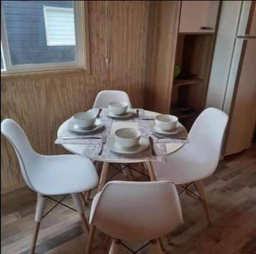 una mesa con sillas blancas y cuencos en Cabañas MR, en Llanquihue