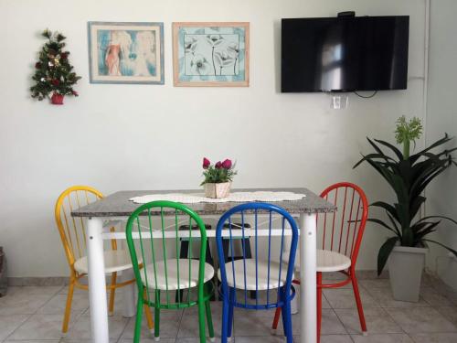 Una mesa de comedor con sillas de colores alrededor. en Apartamento Aconchego da vovó, en Peruíbe
