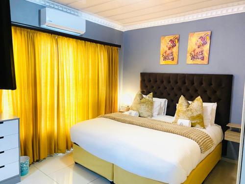 a bedroom with a large bed with yellow curtains at Mnqobi Lifestyle Apartments in Nelspruit