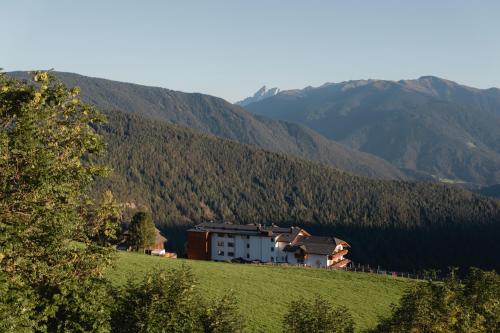 a house on a hill with mountains in the background at Panoramahotel Huberhof in Maranza