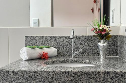 a bathroom counter with a sink and a vase of flowers at Shalom Pousada Capitólio in Capitólio