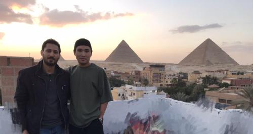 two men standing on top of a wall with the pyramids at Eyad Pyramids view in Cairo